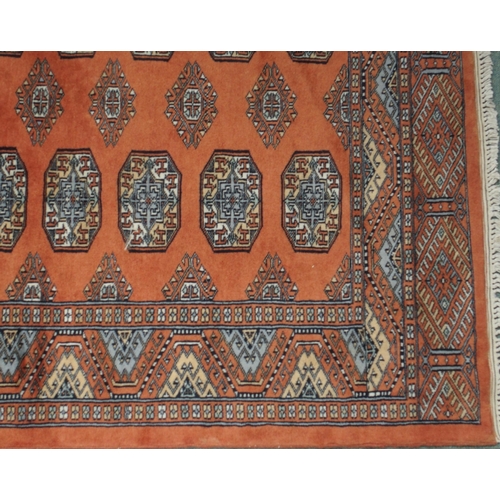 84 - A terracotta ground Bokhara ground rug with all-over lozenge design within multicoloured geometric b... 