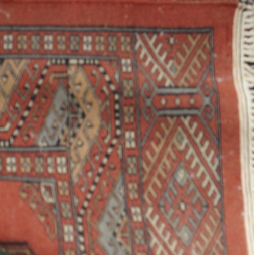 84 - A terracotta ground Bokhara ground rug with all-over lozenge design within multicoloured geometric b... 