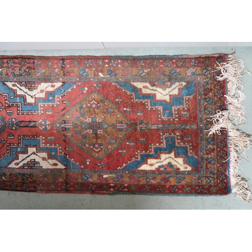 100 - A terracotta ground tribal runner with multicoloured medallions, blue spandrels within geometric bor... 