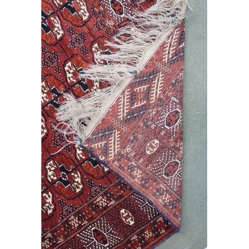 27 - A red ground Bokhara rug with all over lozenge patterned ground within multicoloured geometric borde... 