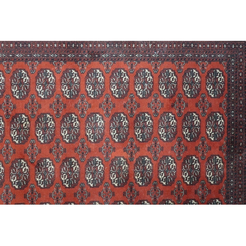 52 - A large red ground Pakistani Bokhara style rug with allover lozenge patterned ground within geometri... 