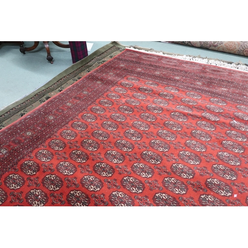 52 - A large red ground Pakistani Bokhara style rug with allover lozenge patterned ground within geometri... 