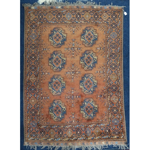 41 - A rust coloured ground Bokhara style rug with lozenge patterned ground within multicoloured geometri... 