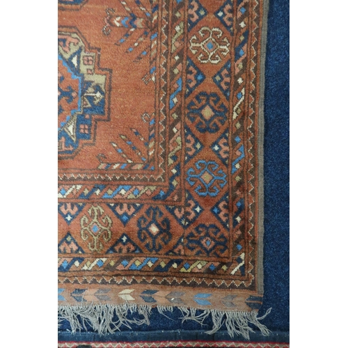 41 - A rust coloured ground Bokhara style rug with lozenge patterned ground within multicoloured geometri... 