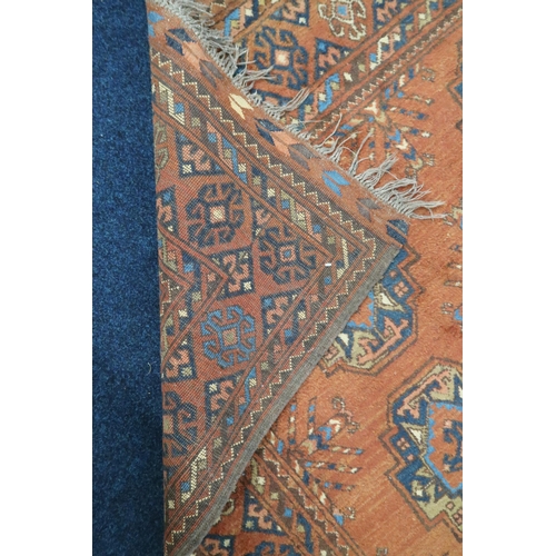 41 - A rust coloured ground Bokhara style rug with lozenge patterned ground within multicoloured geometri... 