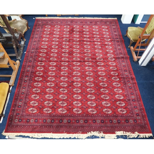 4 - A large red ground Bokhara style rug with all-over lozenge design within multicoloured geometric bor... 