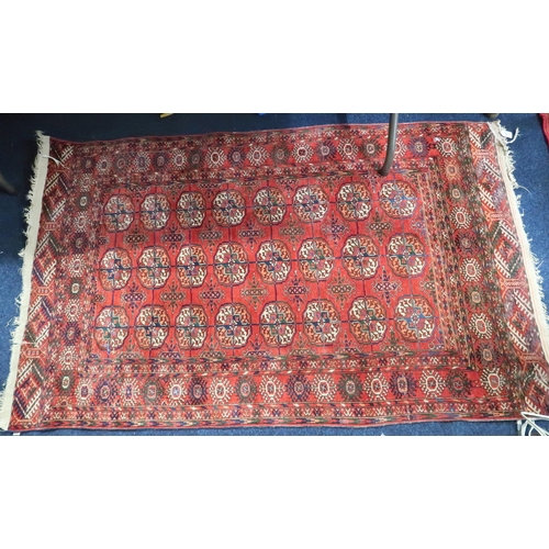 63 - A red ground Bokhara rug with multicoloured all-over lozenge ground within multicoloured geometric b... 