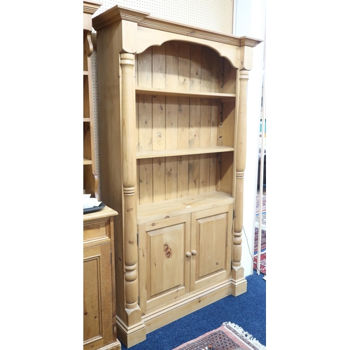 66 - A 20th century pine open bookcase with three open shelves over pair of cabinet doors flanked by colu... 