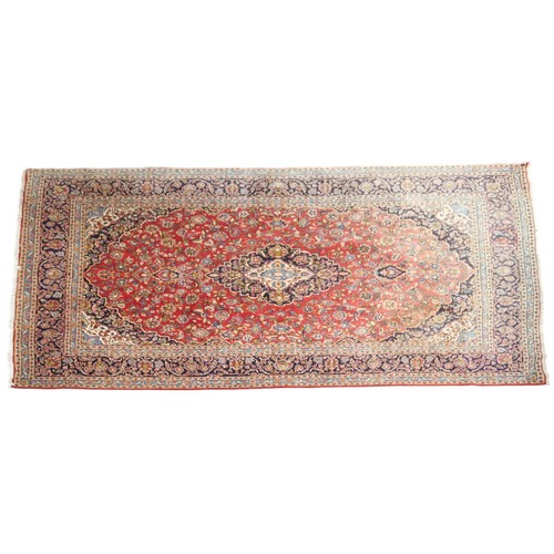 33 - A red ground Keshan rug with dark blue and cream central medallion and matching spandrels on floral ... 