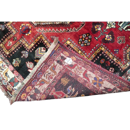 4 - A red ground Hamadan rug with multicoloured geometric diamond medallions and dark spandrels on a geo... 