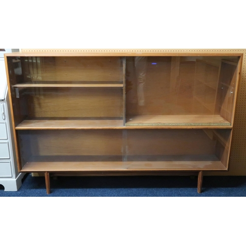 47 - A mid 20th century teak glazed bookcase with two pair of glazed sliding doors on shaped tapering sup... 