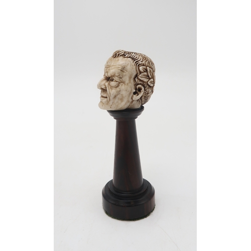 2254 - A CARVED BONE HALF SKULL/ HALF FACEwith a wreath of laurel to the back of the head, upon turned wood... 