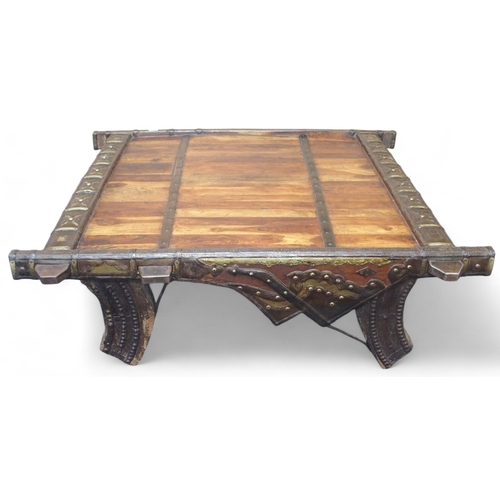 49 - A Indian hardwood coffee table converted from a bull cart with metal bound top and sides on carved s... 