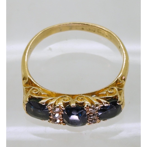 750 - A bright yellow metal three stone sapphire ring, further set with panels of old cut diamonds, with a... 