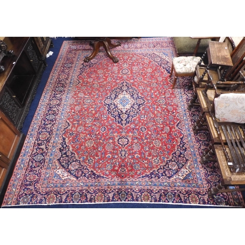 14 - A red ground Keshan rug with dark blue central medallion and matching spandrels on floral patterned ... 