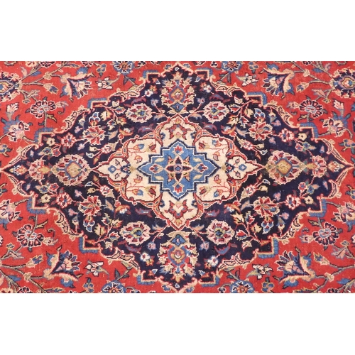 14 - A red ground Keshan rug with dark blue central medallion and matching spandrels on floral patterned ... 