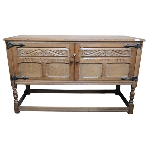 51 - A 20th century oak kitchen dresser base with two carved cabinet doors on turned supports joined by s... 