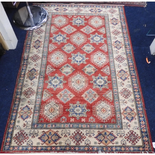 94 - A red ground Kazak rug with multicoloured all over lozenge design with cream geometric border, 186cm... 