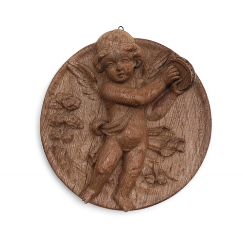 2228 - A LATE 18TH/ EARLY 19TH CENTURY CARVED WOODEN PANELof circular form, carved with a cherub playing a ... 