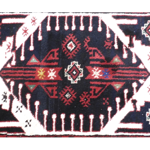 109 - A cream ground Baluch rug with paired dark geometric medallions within red geometric patterned borde... 