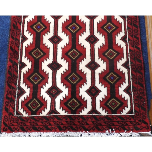 121 - A white ground Baluch rug with dark red geometric ground within red border, 175cm long x 92cm wide