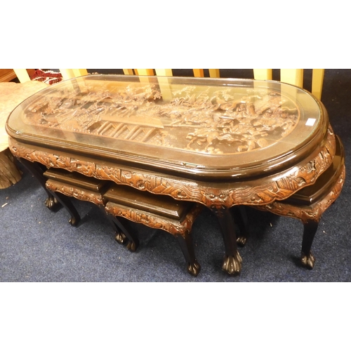 76 - A 20th century Oriental hardwood nesting coffee table with glass oblong top carved with warriors on ... 