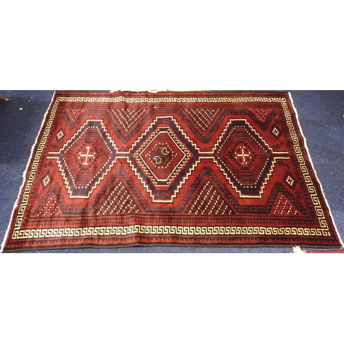 97 - A dark red ground Baluch rug with multicoloured geometric medallions within cream Grecian key style ... 