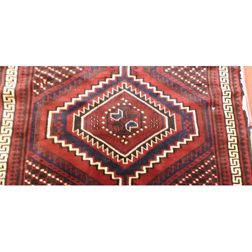 97 - A dark red ground Baluch rug with multicoloured geometric medallions within cream Grecian key style ... 