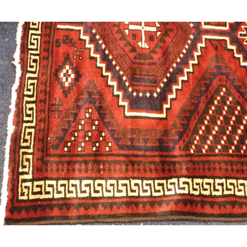 97 - A dark red ground Baluch rug with multicoloured geometric medallions within cream Grecian key style ... 