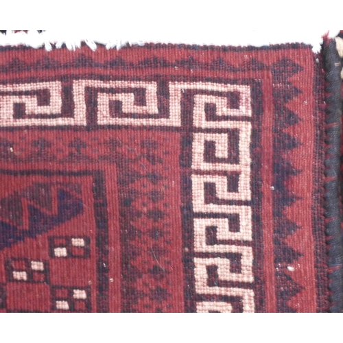 97 - A dark red ground Baluch rug with multicoloured geometric medallions within cream Grecian key style ... 