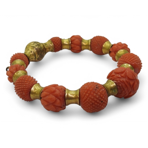 2796 - A CORAL BRACELETeach bead carved with alternate cross hatched pattern or foliate forms, with gold pl... 