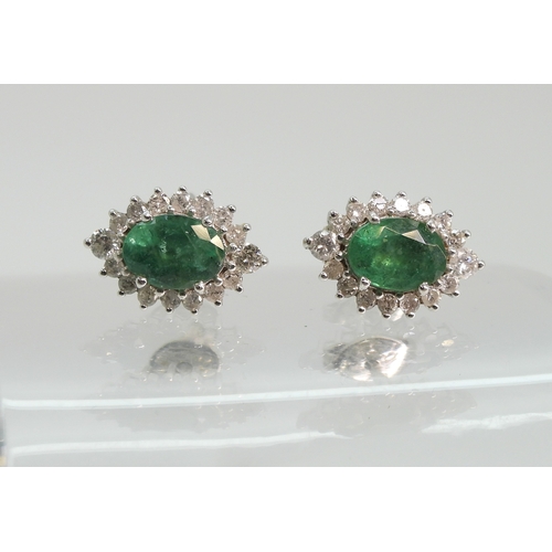 702 - A pair of 18ct white gold emerald and diamond cluster earrings, set with brilliant cut diamonds and ...