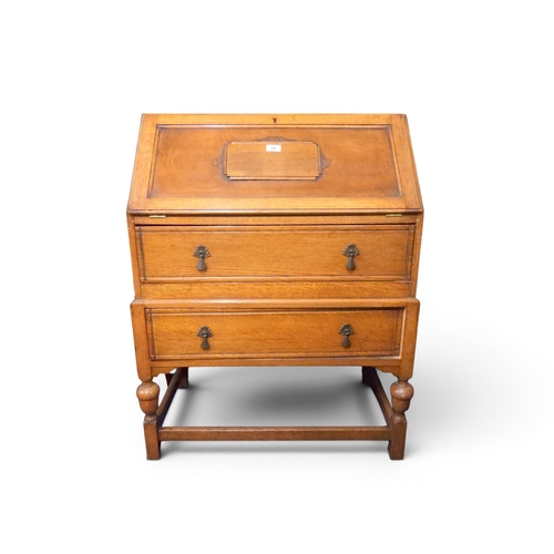 24 - An early 20th oak writing bureau with fall front writing compartment over two long drawers on turned... 
