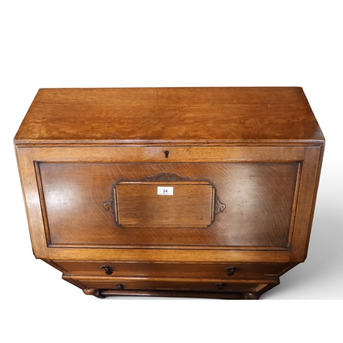24 - An early 20th oak writing bureau with fall front writing compartment over two long drawers on turned... 