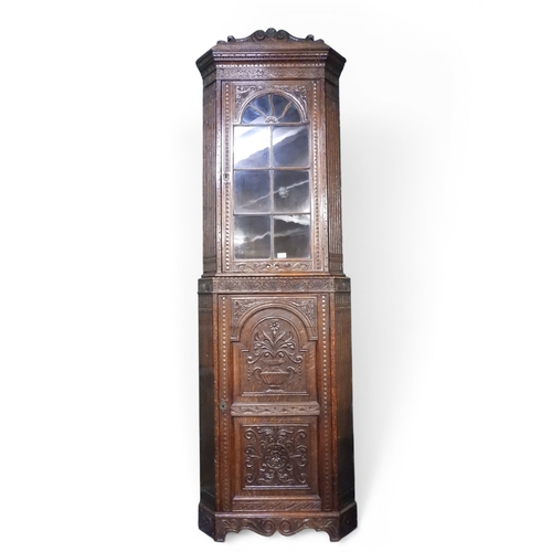 9 - A 19th century oak glazed corner cabinet with carved arched cornice over single beaded glazed door o... 
