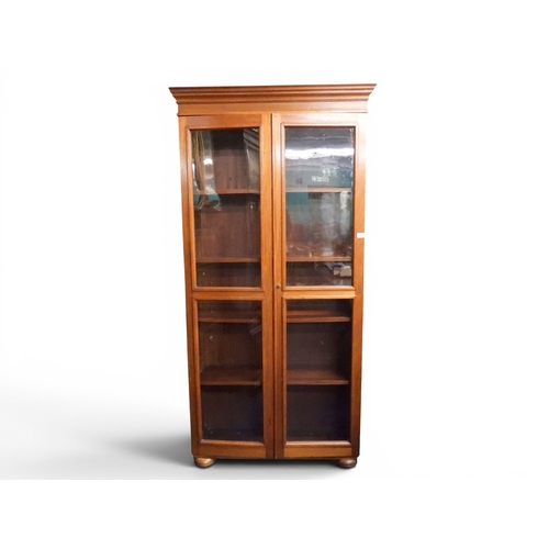 26 - An early 20th century oak glazed bookcase with moulded cornice over pair of glazed doors on bun feet...