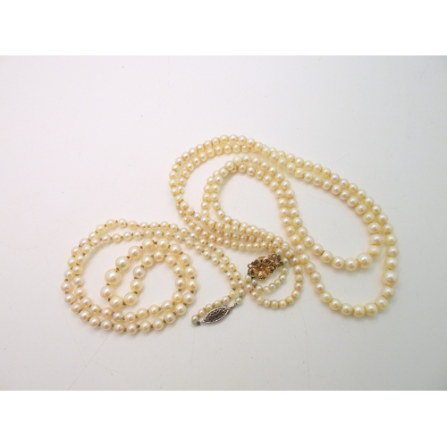 755 - A double string of pearls with a yellow metal flower clasp, and a further single string of pearls wi... 