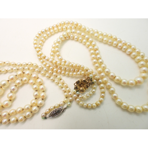 755 - A double string of pearls with a yellow metal flower clasp, and a further single string of pearls wi... 