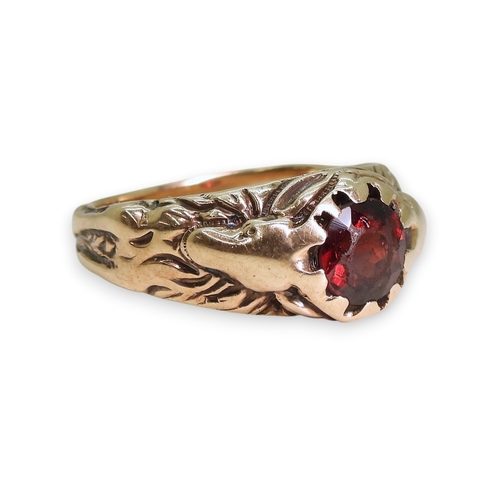 743 - A yellow metal ring set with a garnet with a stag to each shoulder, the antlers make up the claws of... 