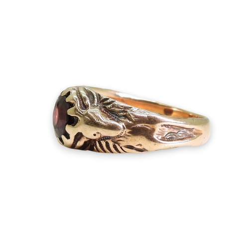 743 - A yellow metal ring set with a garnet with a stag to each shoulder, the antlers make up the claws of... 