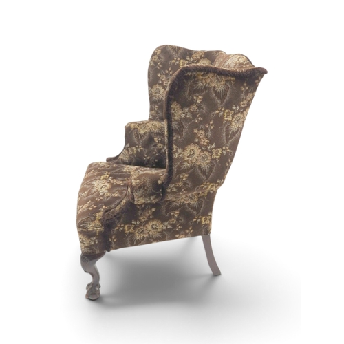 2019 - AN EARLY 20TH CENTURY BROWN FLORAL UPHOLSTERED WINGBACK ARMCHAIR&nbsp;with rolled arms on serpentine... 