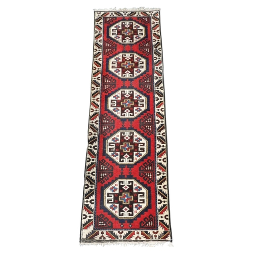 5 - A red ground Heriz runner with five octagonal multicoloured geometric medallions within multicoloure... 