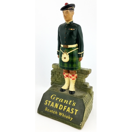 83 - GRANTâS STANDFAST SCOTCH WHISKY BAR FIGURE. 10ins tall rubberoid uniformed highlander stooad atop ... 