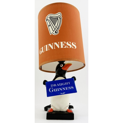 202 - GUINNESS PENGUIN & LAMP SHADE BAR TOP LAMP. 14.6ins tall. Multi coloured penguin lamp base, holding ... 