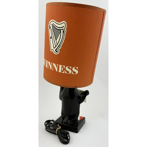 202 - GUINNESS PENGUIN & LAMP SHADE BAR TOP LAMP. 14.6ins tall. Multi coloured penguin lamp base, holding ... 