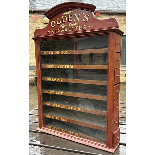 85 - OGDENS CIGARETTES DISPENSING CABINET. 31.5 x 22 x 5.25ins. Brown painted wood, shapely finial with g... 