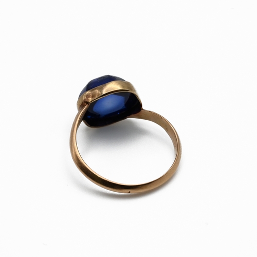 102 - A gold single stone synthetic sapphire ring, finger size M unmarked.