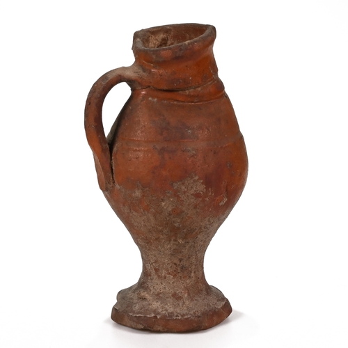 513 - A small naive earthenware jug with pie crust foot. Dates c15th-17th Century. An old label to the und... 