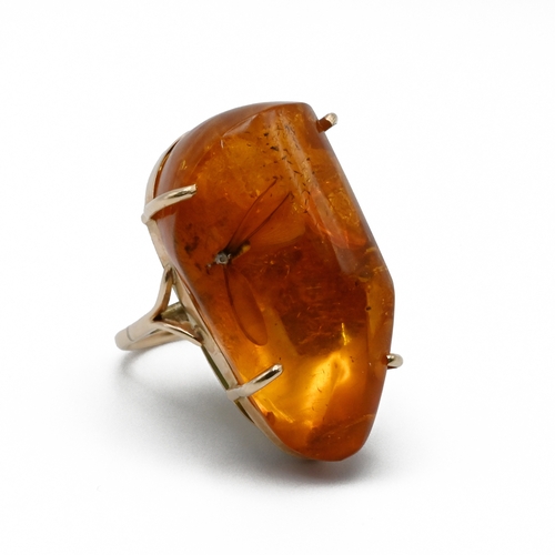 84 - An gold amber ring, the large asymmetrical stone having a bug inclusion, the shank unmarked, in a Sa... 