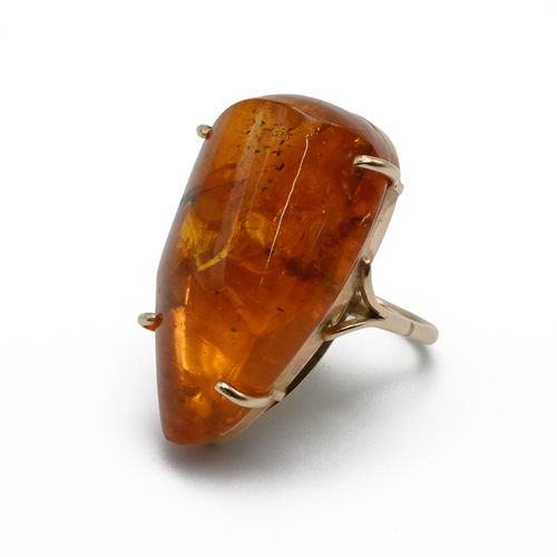 84 - An gold amber ring, the large asymmetrical stone having a bug inclusion, the shank unmarked, in a Sa... 